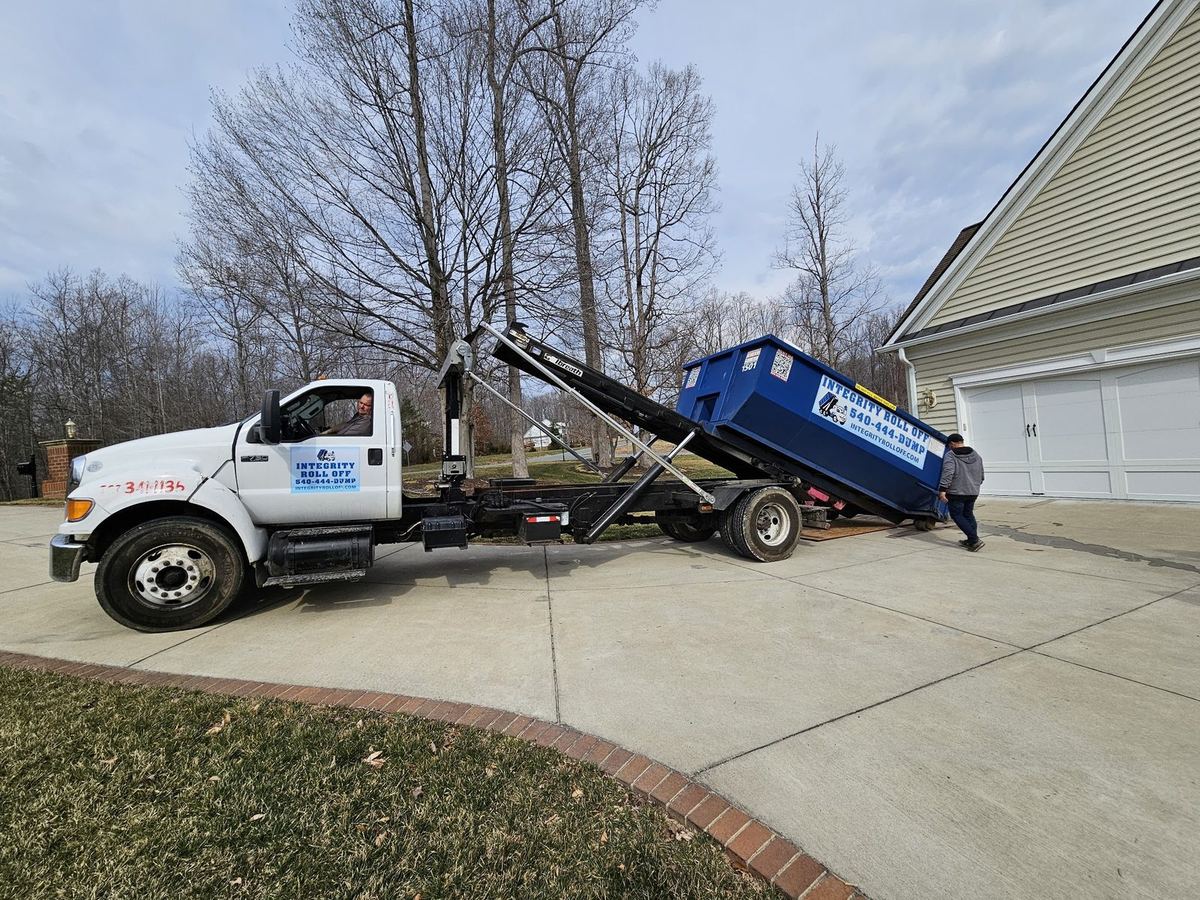 Integrity Roll Off truck rolling a dumpster off in a customer’s driveway