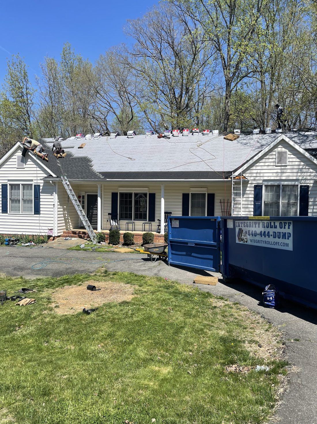 Roofing crew mid tear-off with an Integrity Roll Off dumpster at the house